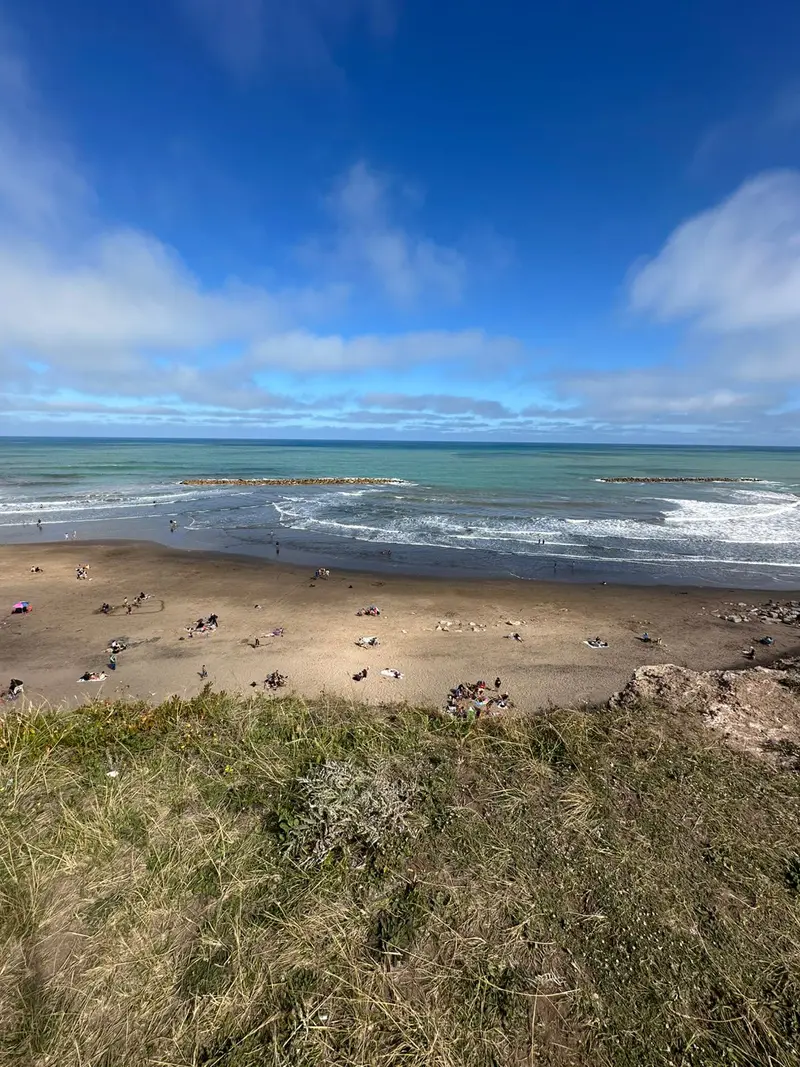 Vista del mar desde lo alto del acantilado, con la playa y escolleras.