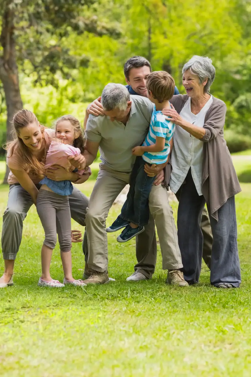 Tres generaciones de una familia se ríen juntas sobre el césped de un parque.
