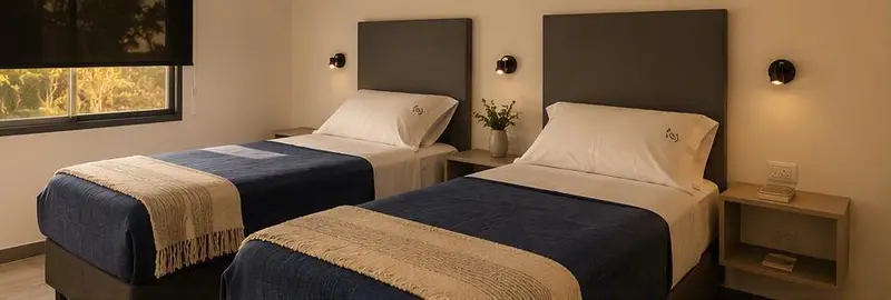 Dormitorio con dos camas, respaldos grises, acolchados azules y ventana al jardín.